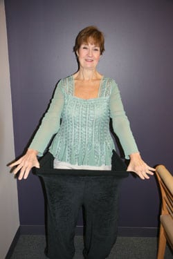Peggy After 221 pounds medical surgical weight loss posing in old pants