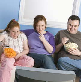 heavy family eating junk food on couch watching tv